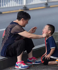 大妈抽着烟坐在路边 让孙子学狗爬从地上叼蛇玩…